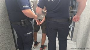 Dwaj policjanci prowadzą zatrzymanego mężczyznę skutego w kajdanki.