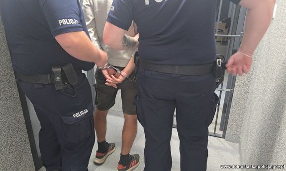 Dwaj policjanci prowadzą zatrzymanego mężczyznę skutego w kajdanki.