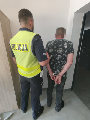 Zatrzymany mężczyzna w kajdankach prowadzony przez policjanta.