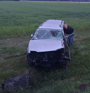Rozbity pojazd na skraju pola. Do wnętrza zagląda nieumundurowany policjant.