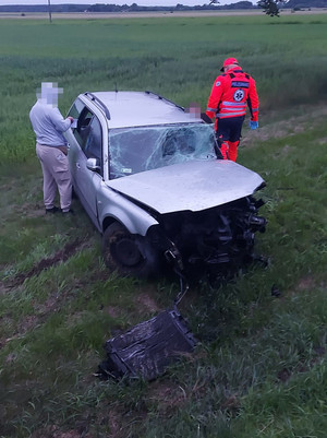 Rozbity pojazd na skraju pola. Przy pojeździe nieumundurowany policjant i ratownik medyczny.