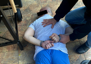 Zatrzymany leży na podłodze zakuty w kajdanki, trzyma go policjant.