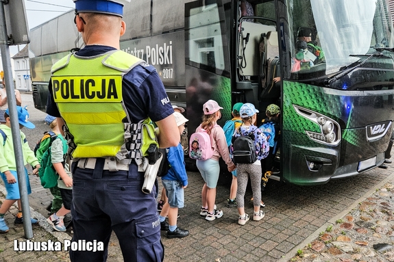 Policjant stoi przy autokarze, do którego wchodzą małe dzieci.