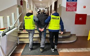 Dwaj funkcjonariusze prowadzą zatrzymanego mężczyznę.
