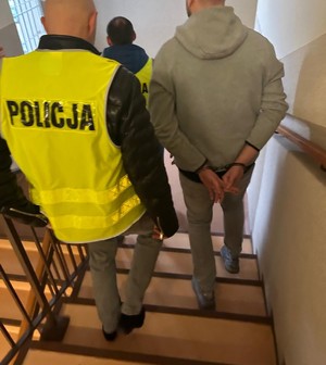 Dwaj funkcjonariusze prowadzą zatrzymanego mężczyznę.