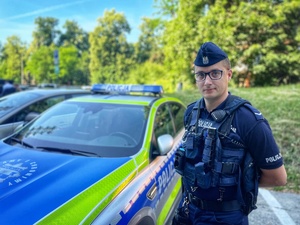 Policjant stoi przy radiowozie.