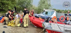 Służby ratują życie, obok łódź policyjna i strażacka.