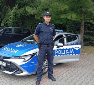 Umundurowany policjant przy radiowozie.