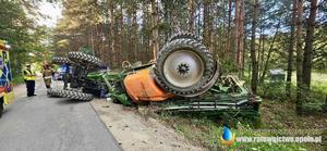 Ciągnik z opryskiwaczem lezący na boku.