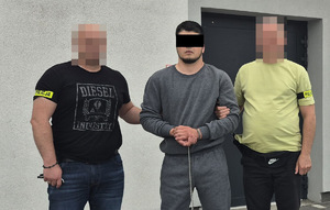 Zatrzymany mężczyzna prowadzony przez dwóch nieumundurowanych policjantów. Widok - z przodu.