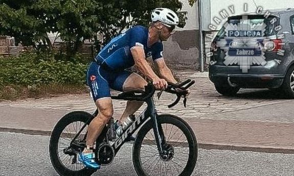 Na zdjęciu mężczyzna jadący rowerem. W tle samochód