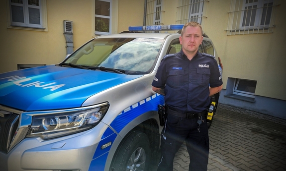 Policjant stoi przy radiowozie.