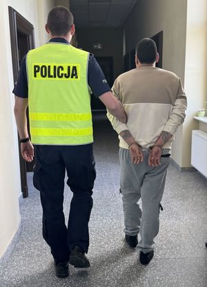 Policjant prowadzi korytarzem zatrzymanego mężczyznę.
