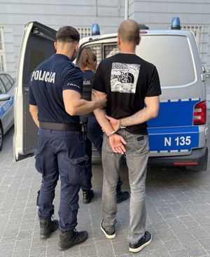 Policjant z zatrzymanym przy radiowozie.