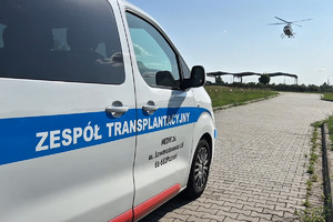 Furgonetka zespołu transplantacyjnego, w oddali nadlatujący policyjny śmigłowiec.