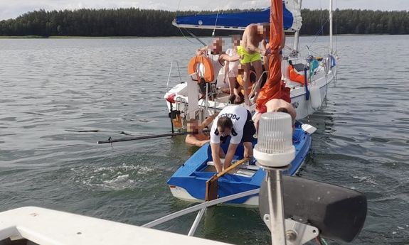 Żaglówki na jeziorze - policjant wylewa wodę z łodzi.