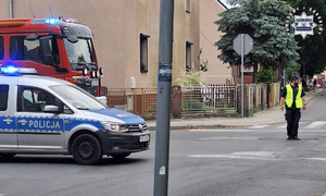 Policjant zabezpiecza miejsce  pożaru hali w Kędzierzynie - Koźlu. Z boku widoczny radiowóz policyjny i wóz straży pożarnej.