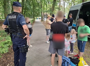 Policjanci przy radiowozie. Obok stoi kilka osób dorosłych i kilkoro dzieci.