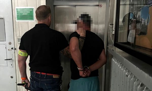 Policjant prowadzi zatrzymanego w kajdankach.