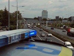 Z przodu widać belkę policyjnego radiowozu z napisem Policja. Z tyłu widok na ulicę miasta.