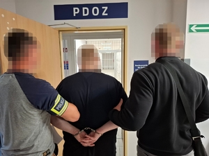 Dwaj policjanci prowadzą zatrzymanego mężczyznę.