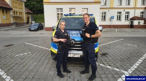 Dwoje umundurowanych policjantów przed radiowozem.
