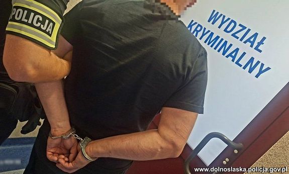 Policjant prowadzi zatrzymanego skutego w kajdanki.