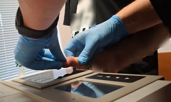 policjant pobiera odciski palców zatrzymanemu.