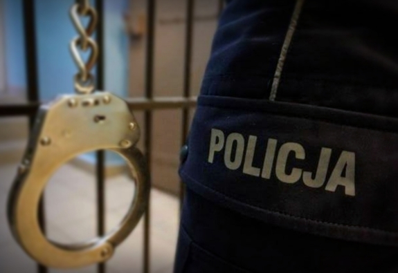 Policjant trzyma kajdanki na tle krat.