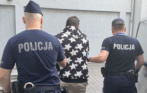 Policjanci prowadzą do radiowozu zatrzymanego.