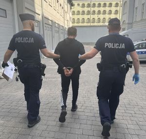 Policjanci prowadzą do radiowozu zatrzymanego.