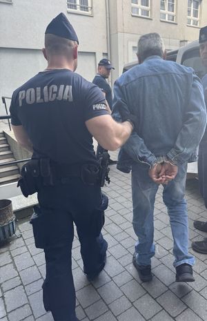 Policjanci prowadzą do radiowozu zatrzymanego.