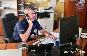 Policjant dyżurny siedzi przy biurku rozmawiając przez telefon.