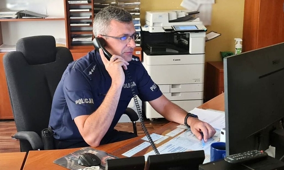 Policjant dyżurny siedzi przy biurku rozmawiając przez telefon.