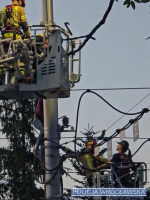 policjanci i strażacy stoją na podnośniku przy latarni.