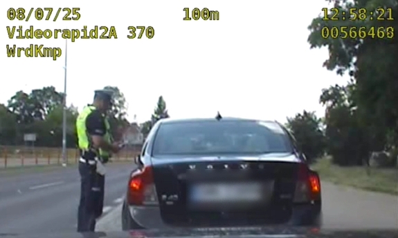 Policjant stoi przy zatrzymanym samochodzie w trakcie kontroli drogowej.