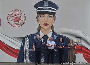 Mural przedstawiający wizerunek policjantki i osoby przecinające wstęgę.