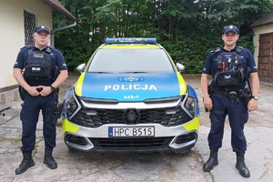 Dwaj policjanci stoją przy radiowozie.