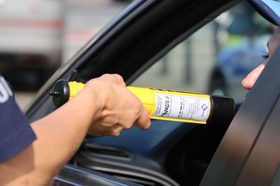 Dłoń policjanta, w której trzyma alcoblow - urządzenie do pomiaru stanu trzeźwości - i podaje kierującemu pojazdem, a ten w nie dmucha.