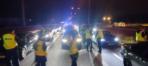 Na ulicy oświetlone pojazdy i policjanci kontrolujący auta. Czynności wykonywane w porze nocnej.