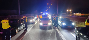 Na ulicy oświetlone pojazdy i policjanci kontrolujący auta. Czynności wykonywane w porze nocnej.