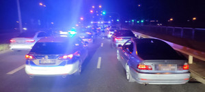 Na ulicy oświetlone pojazdy i policjanci kontrolujący auta. Czynności wykonywane w porze nocnej.