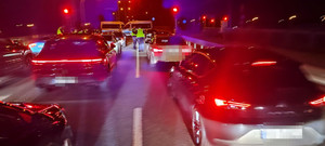 Na ulicy oświetlone pojazdy i policjanci kontrolujący auta. Czynności wykonywane w porze nocnej.
