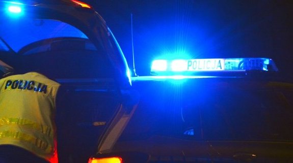 Pora nocna. Policjant w kamizelce z napisem Policja i policyjny radiowóz.