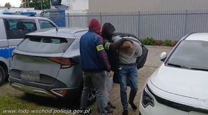 Dwóch policjantów prowadzi zatrzymanego mężczyznę.