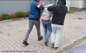 Dwóch policjantów prowadzi zatrzymanego mężczyznę.