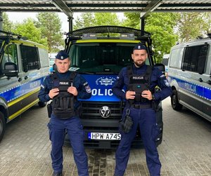 policjanci stoją przed radiowozem.
