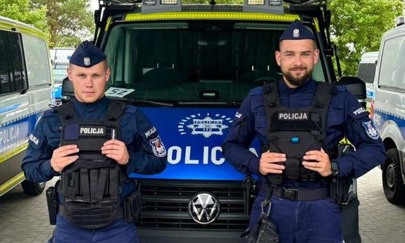 policjanci stoją przed radiowozem.