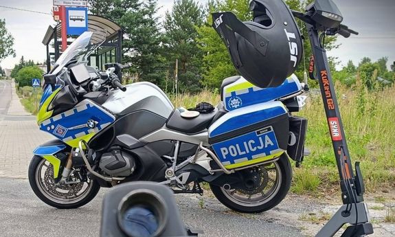 policyjny motocykl, obok stoi hulajnoga elektryczna.