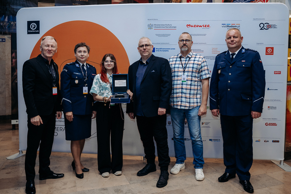 Dwoje umundurowanych policjantów, kobieta i trzech mężczyzn w garniturach.
